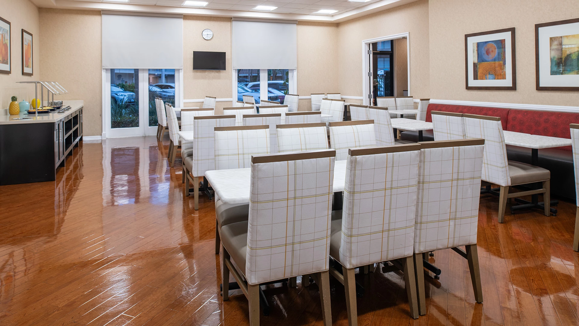 A dining area with white chairs, wooden tables, and booth seating.