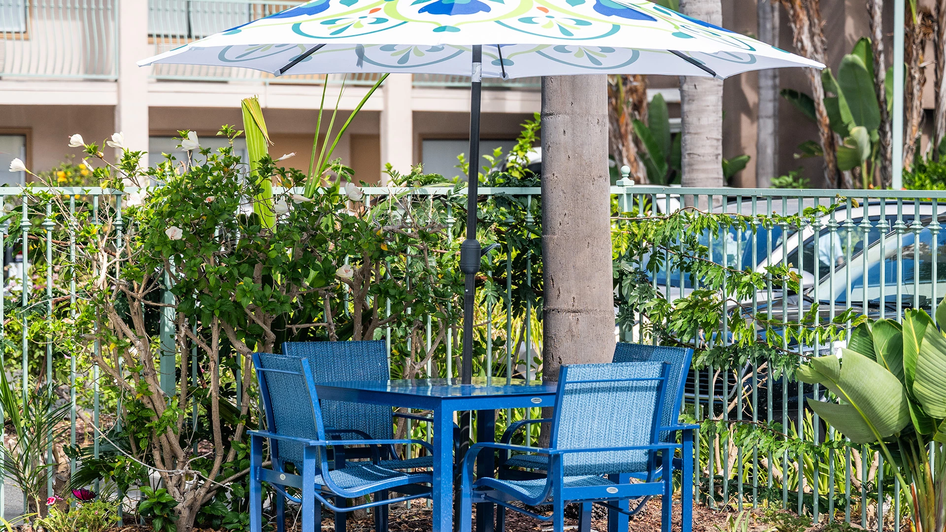 A blue patio set with an umbrella in a fenced outdoor area with plants.