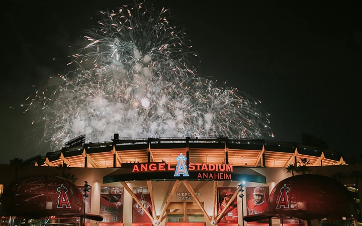 A nighttime view of the exterior of Angel Stadium in Anaheim with fireworks exploding above it.