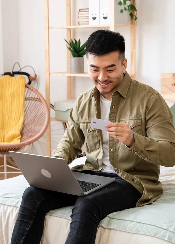 a man sitting on a bed holding a card and using a laptop