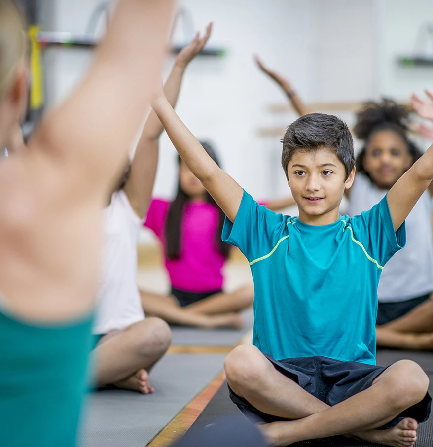 a group of kids sitting on mats with their hands up