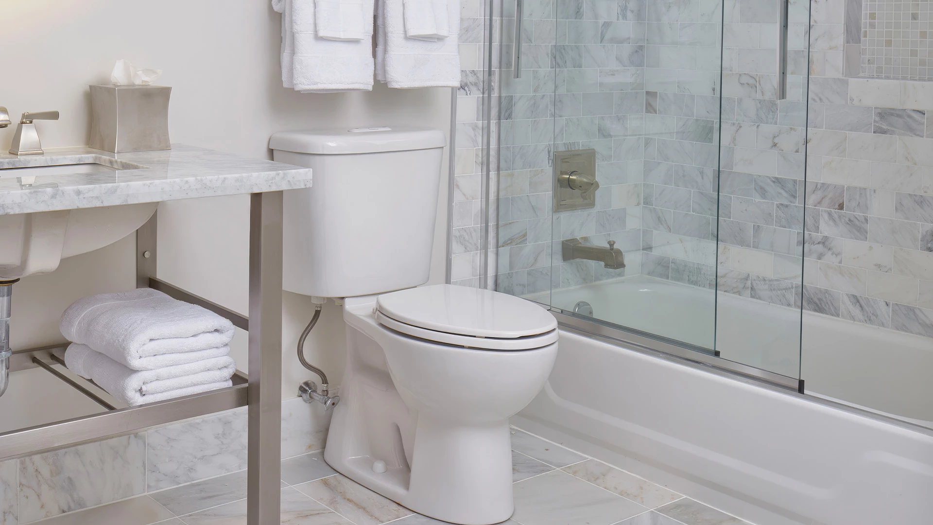 A clean bathroom with a toilet, shower, bathtub, and marble countertop.
