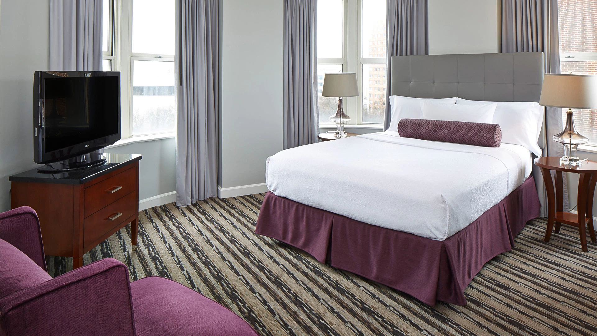 A hotel room with a bed, TV, chair, and window.
