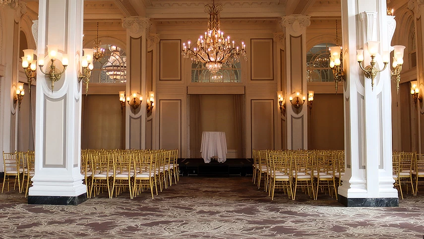 A large, ornate meeting room with a stage, gold chairs, and a chandelier.