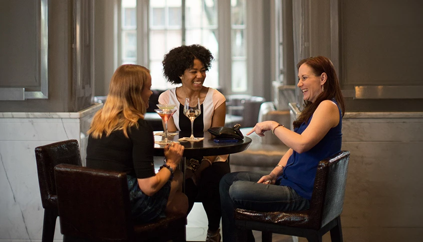 Three women sitting at a table in a hotel lobby, laughing and chatting.