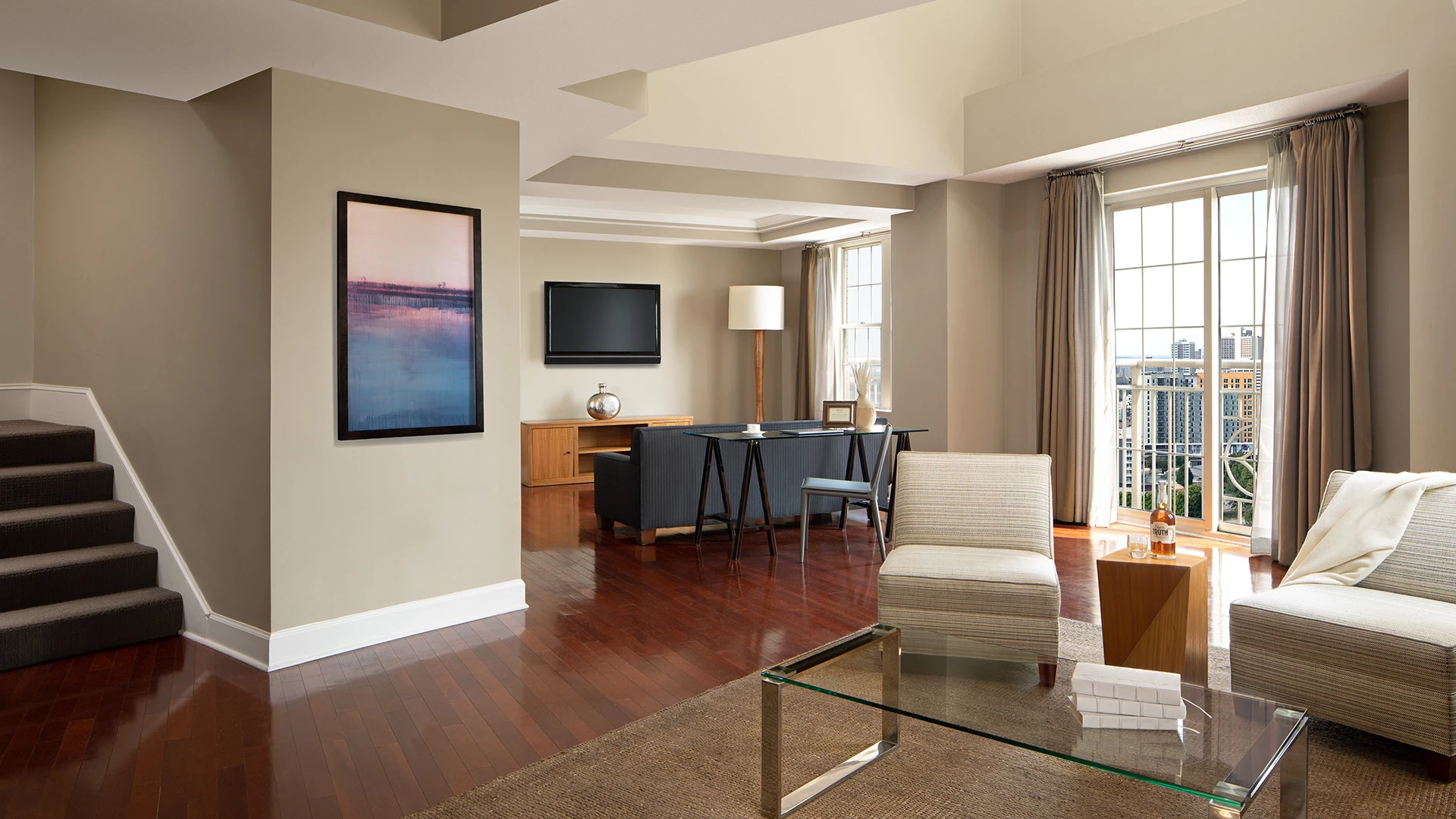 A hotel lobby with a sofa, coffee table, TV, desk, and window.