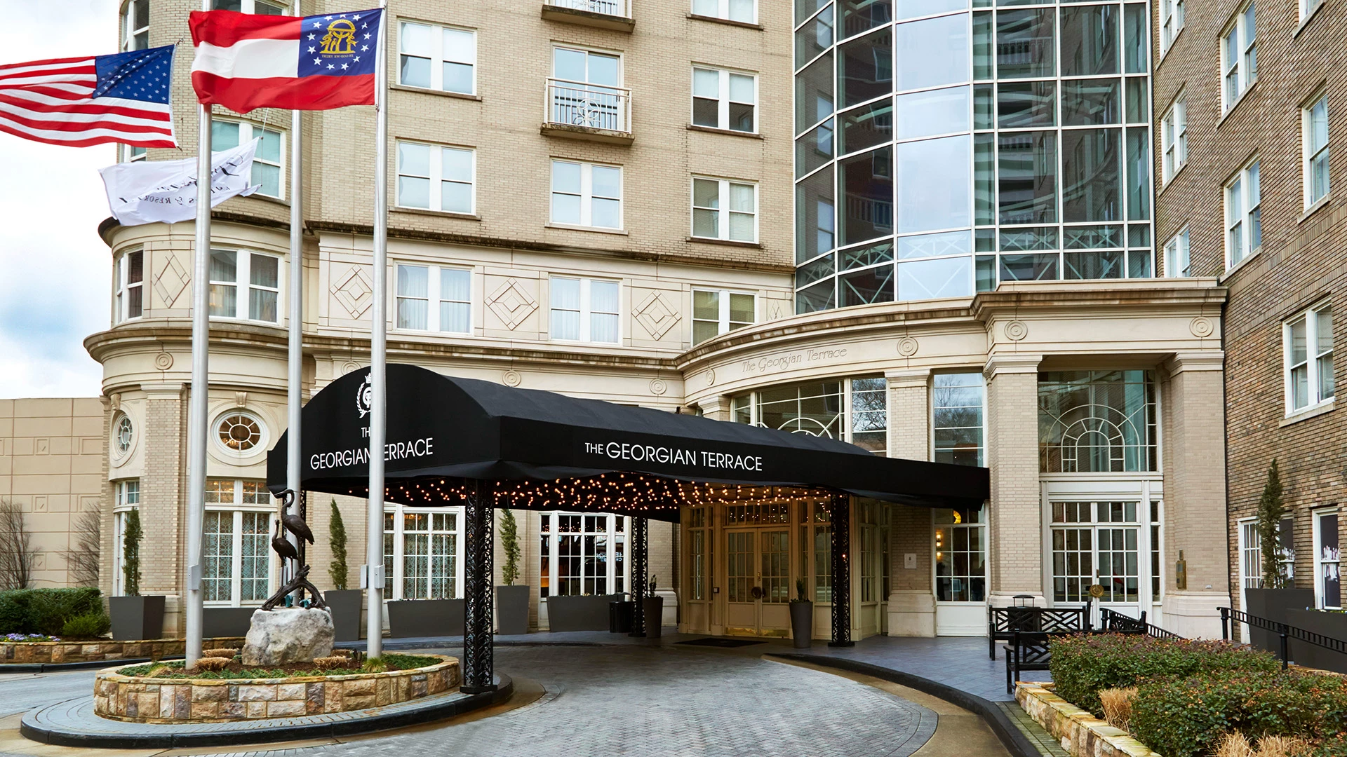 A beige brick building with a black awning over the entrance, flags flying in front, and a statue near the flags.