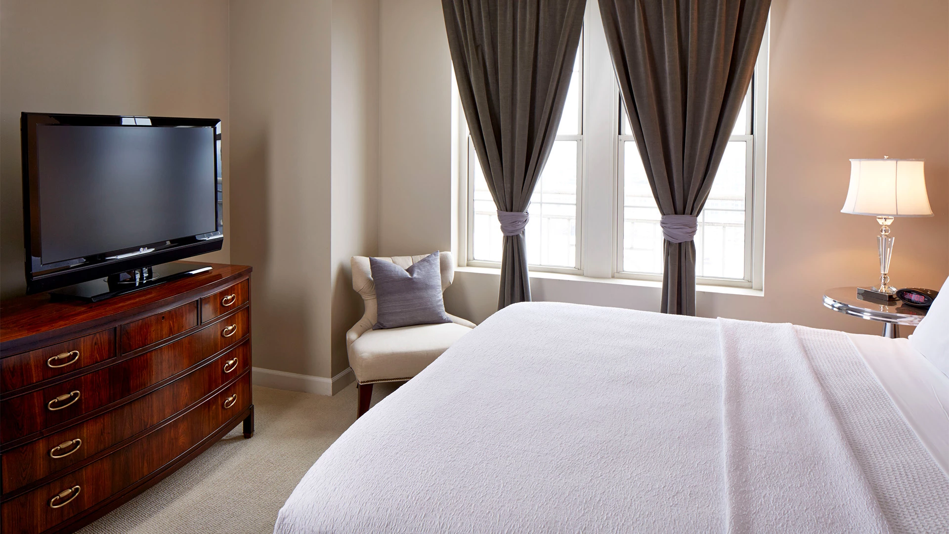A hotel room with a bed, dresser, TV, chair, and window