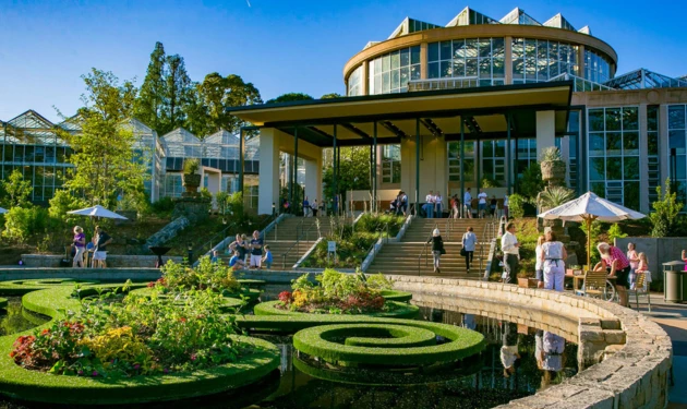 A large, modern building with a curved glass facade and a landscaped garden in the foreground.