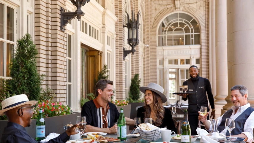 A group of people dining outdoors at a table with wine glasses and bottles.