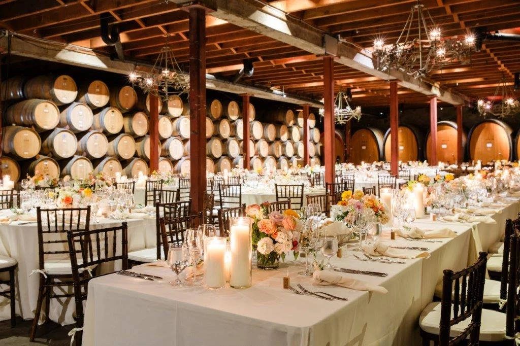 a room with tables and chairs with wine barrels in the background