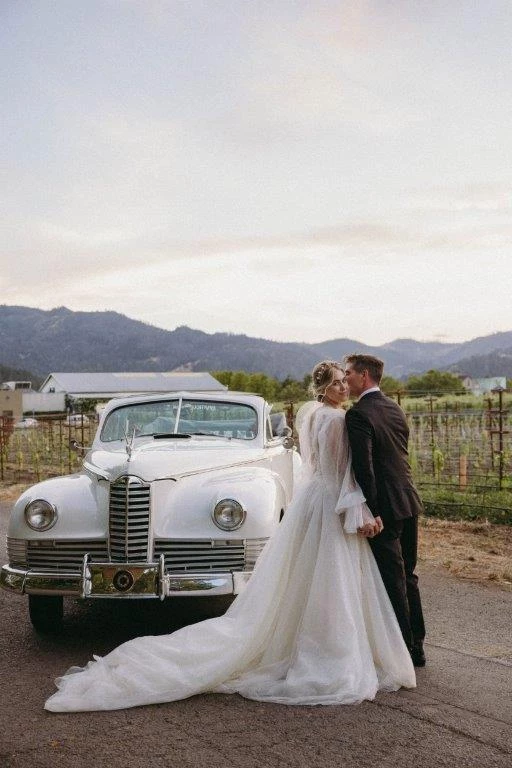 a man and woman in wedding dress and suit standing next to a car
