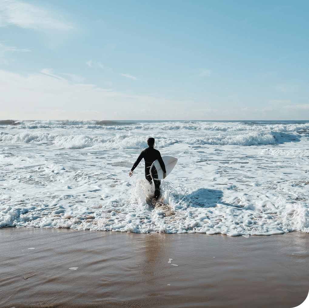 a man walking into the ocean with a surfboard