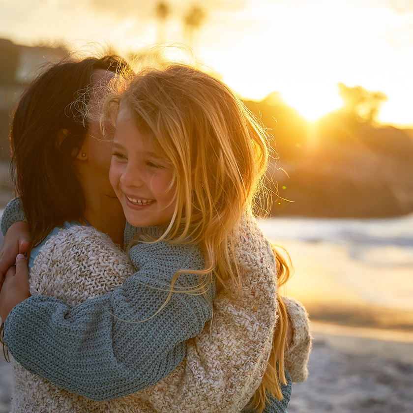 a woman and a girl hugging on a beach