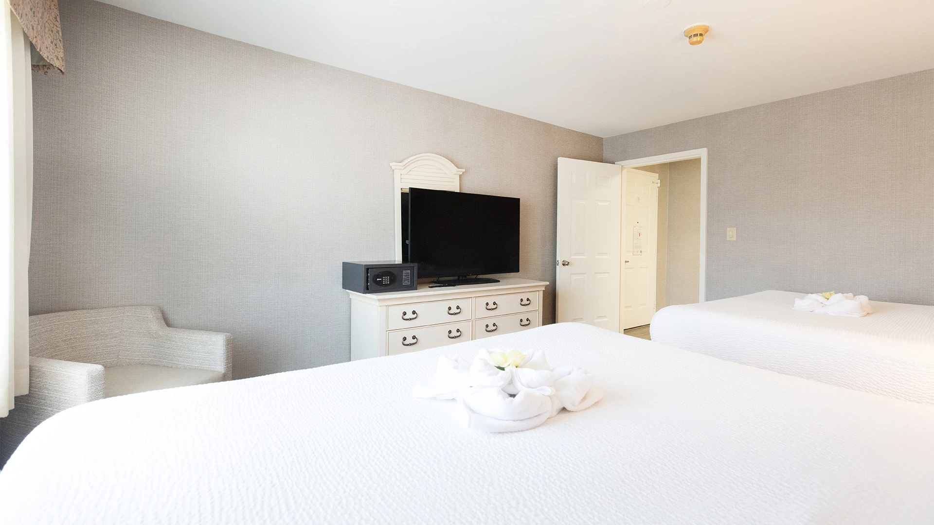 A hotel room with two beds, a TV on a dresser, and a chair.