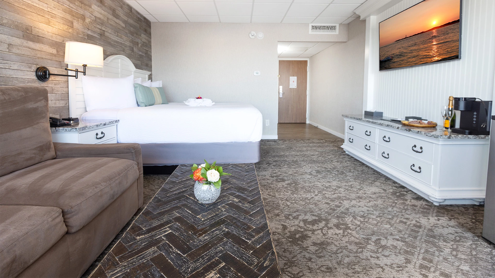 A wide view of a hotel room with a large bed, sofa, coffee table, TV, and dresser.