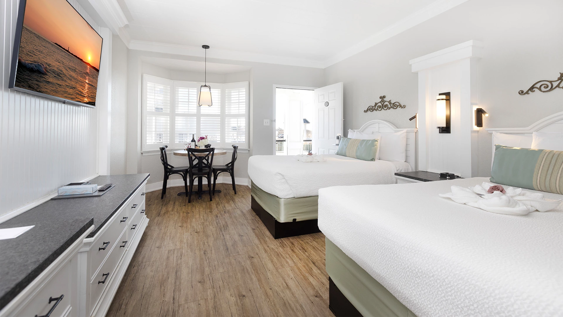 A wide view of a hotel room with two beds, a dining area, and a window.