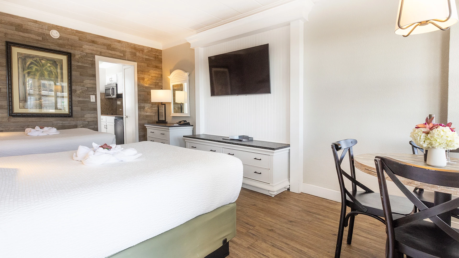 A hotel room with two beds, a desk, TV, and kitchenette.