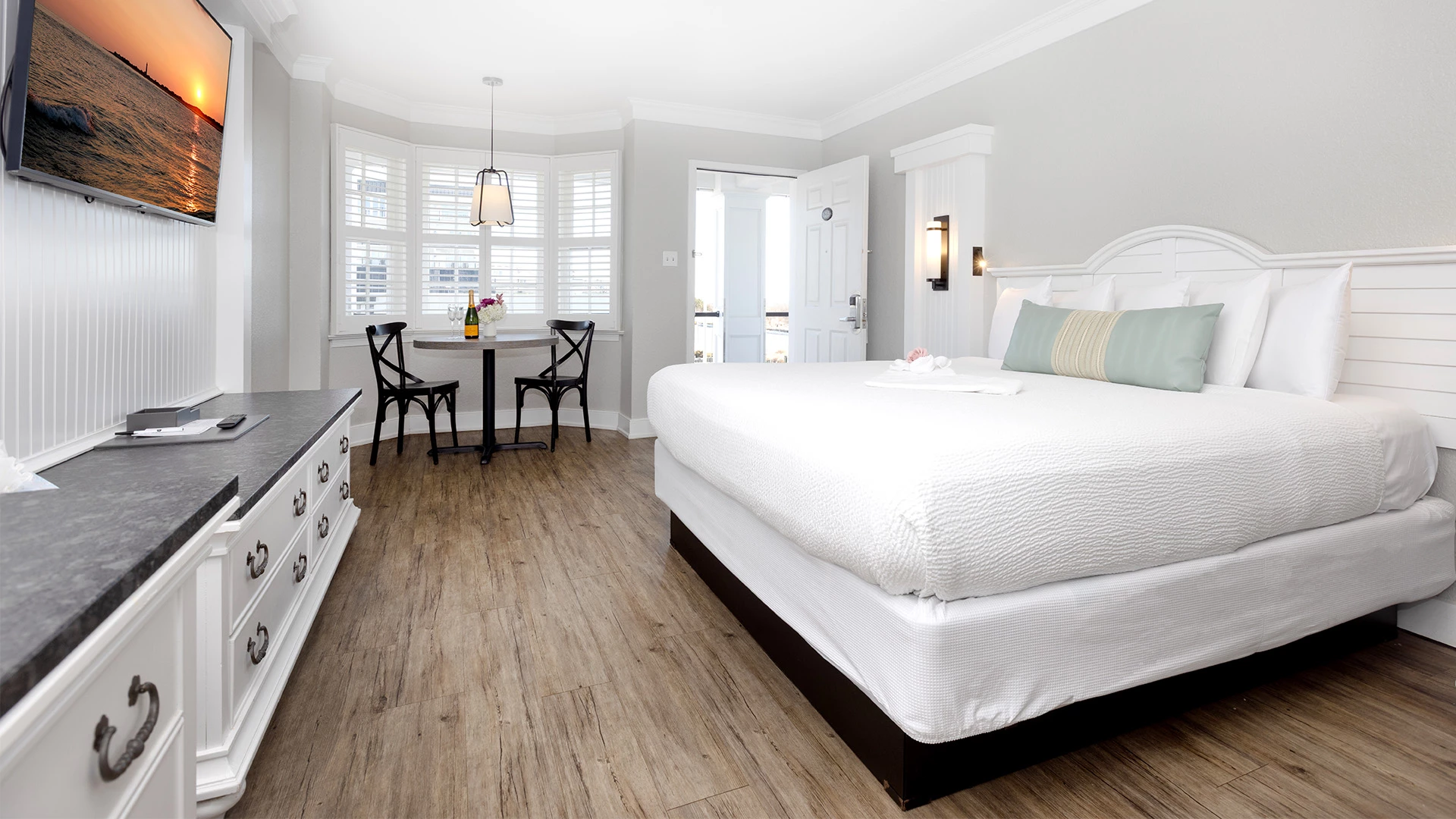 A large hotel room with a king-sized bed, TV, dresser, dining area, and door