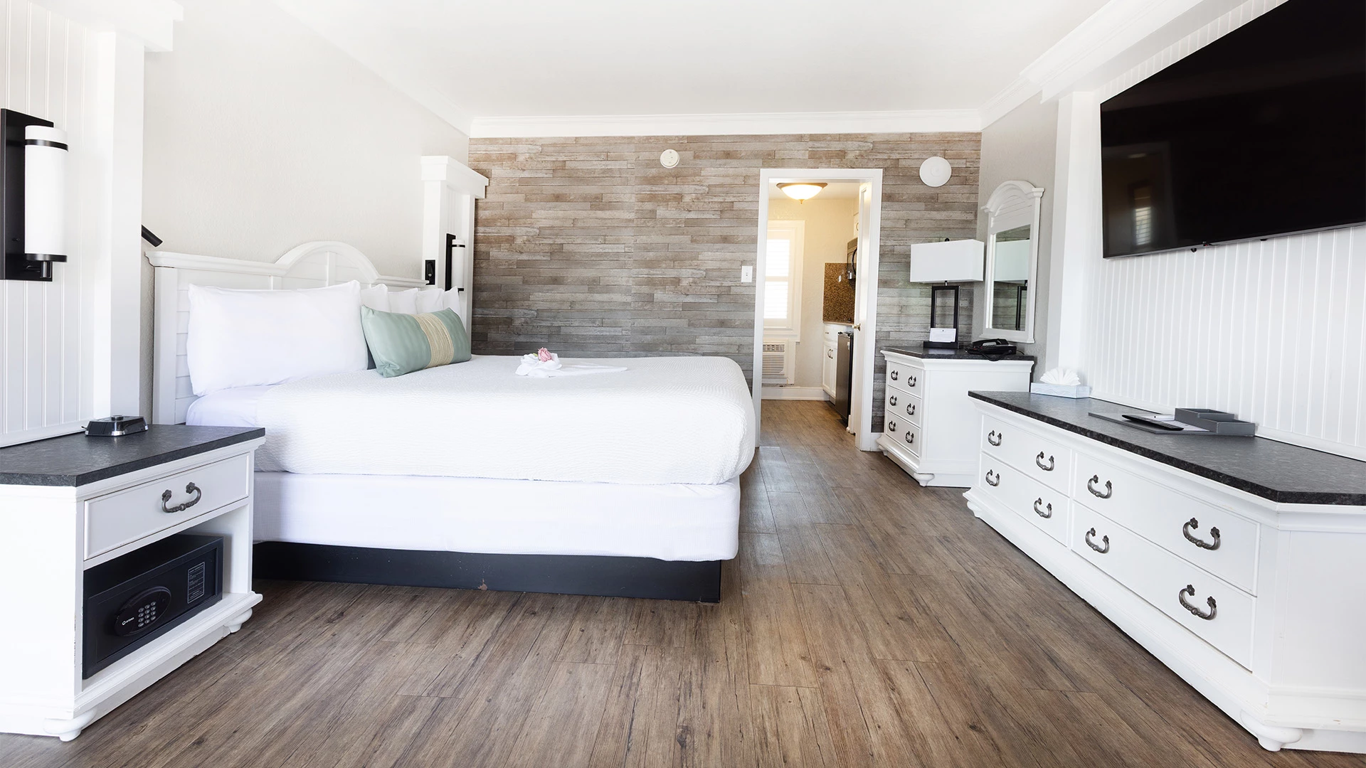 A wide view of a hotel room with a bed, TV, kitchenette, and safe.