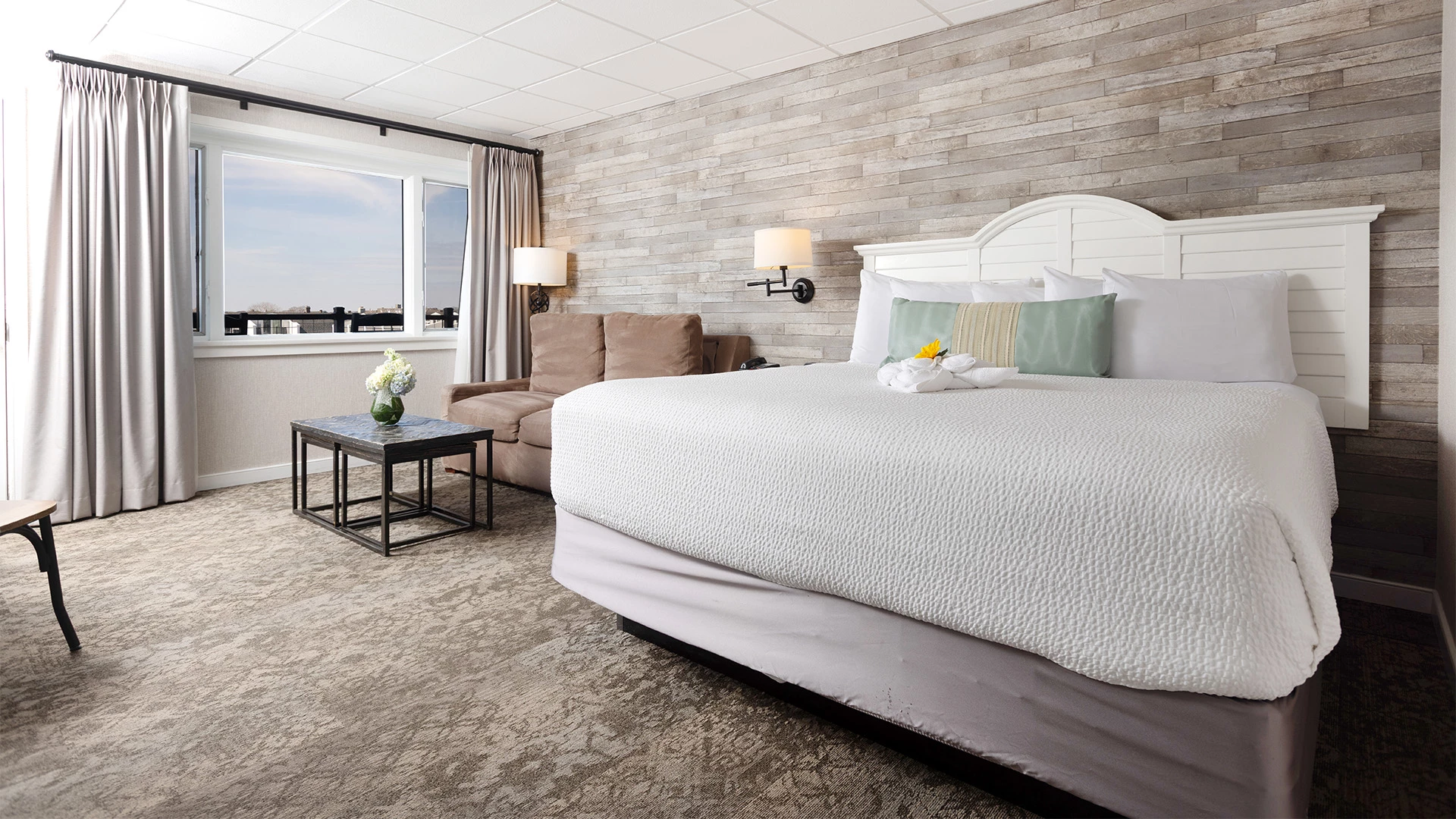 A hotel room with a large bed, a sofa, a coffee table, and a window.