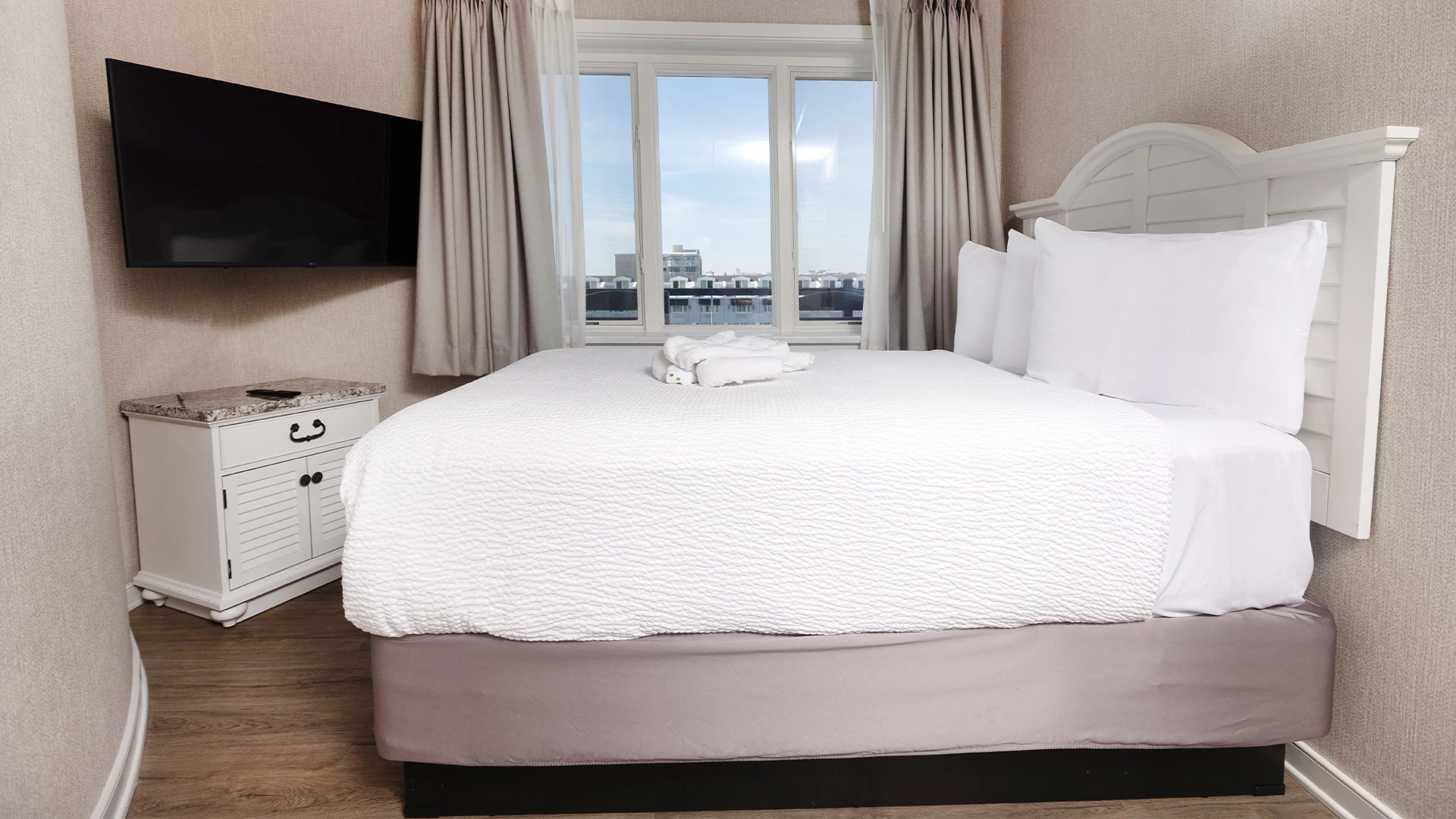 A hotel room with a bed, TV, and window