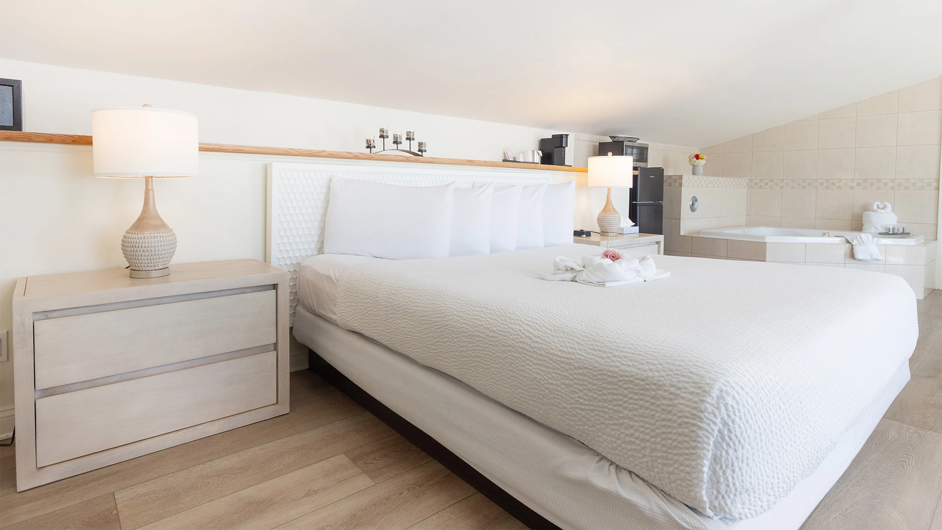 A hotel room with a large bed, nightstand, and jacuzzi in the background.