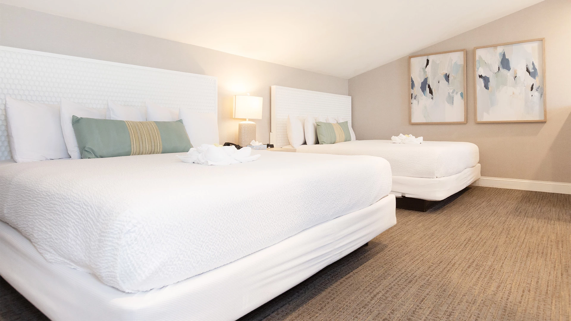 A hotel room with two beds, a lamp, and paintings on the wall.