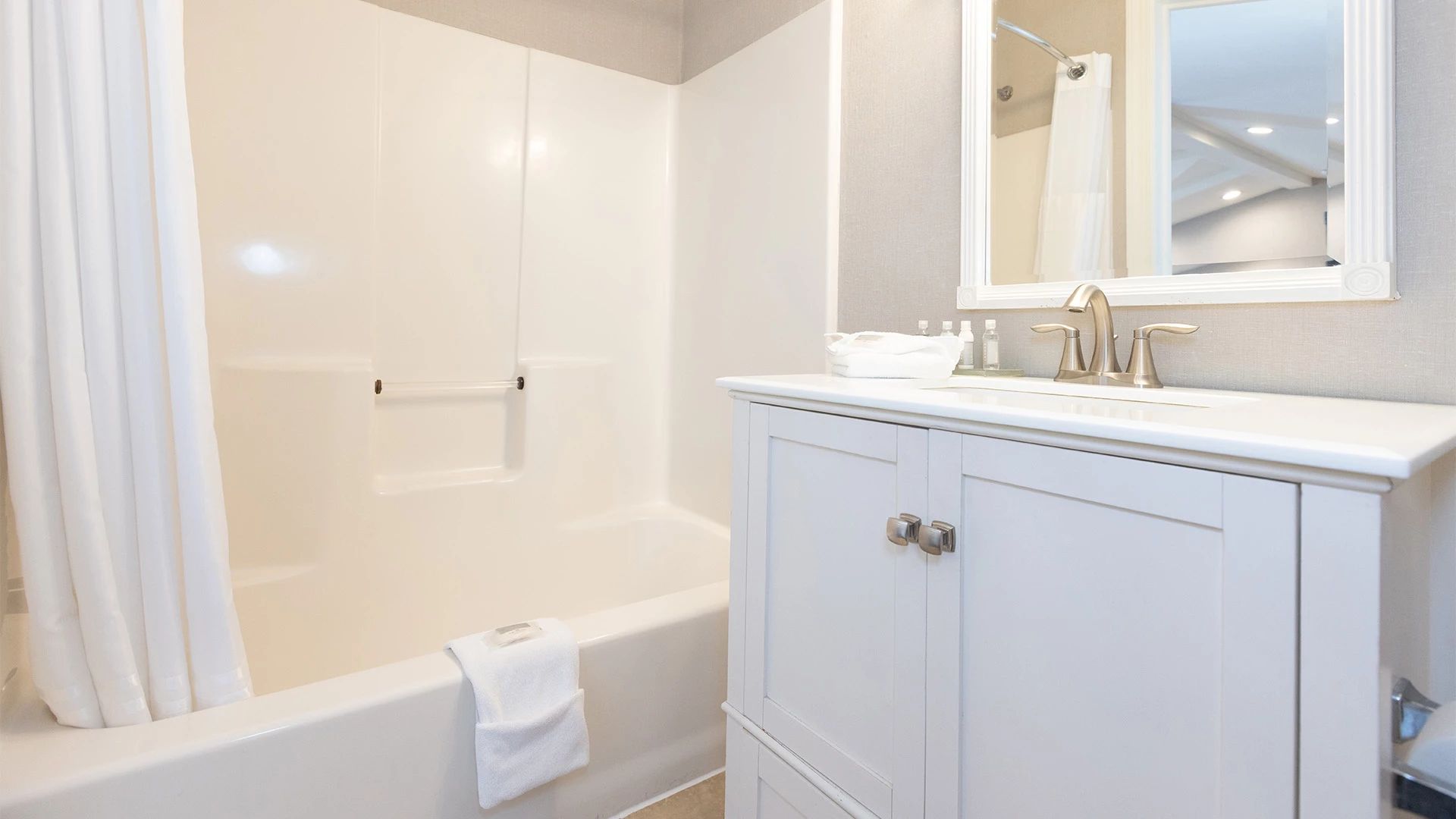 A clean bathroom with a white cabinet, sink, mirror, bathtub, and shower curtain.