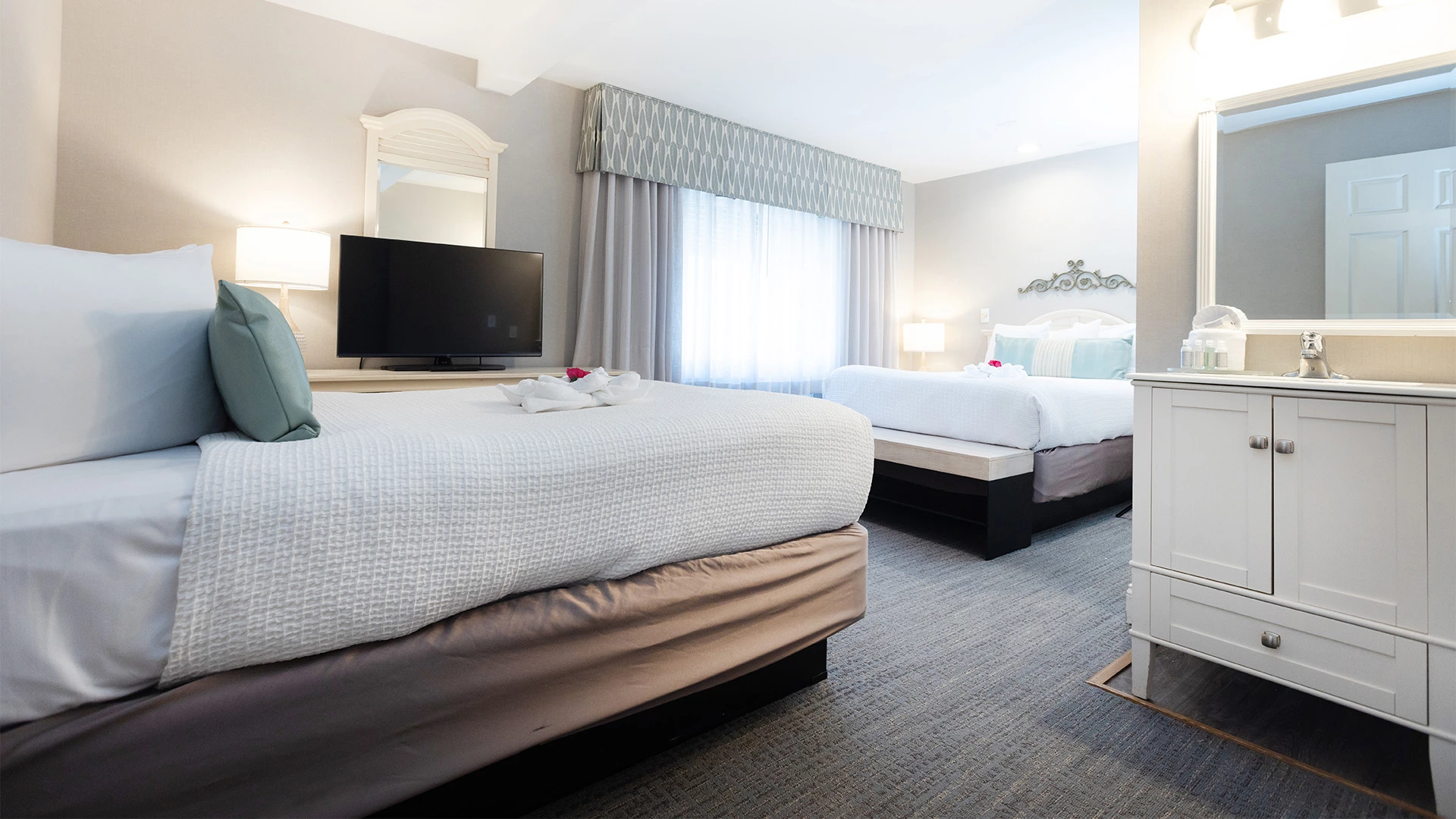 A hotel room with two beds, a TV, and a dresser.