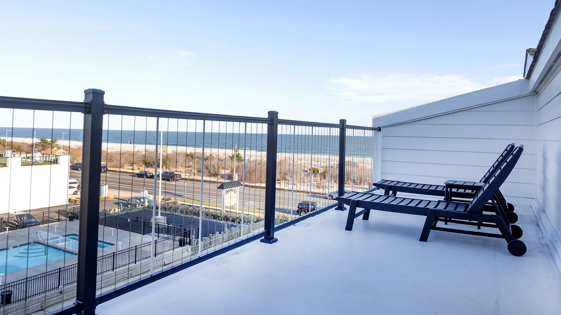 A balcony with lounge chairs and a railing overlooking the ocean and a pool.