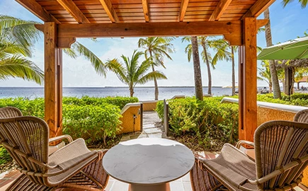 a table and chairs outside with a view of the ocean and palm trees