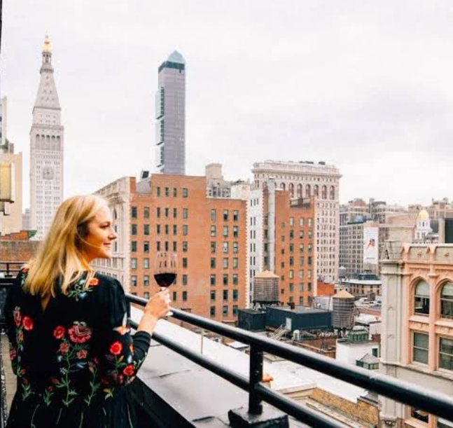 a woman holding a glass of wine looking at a city