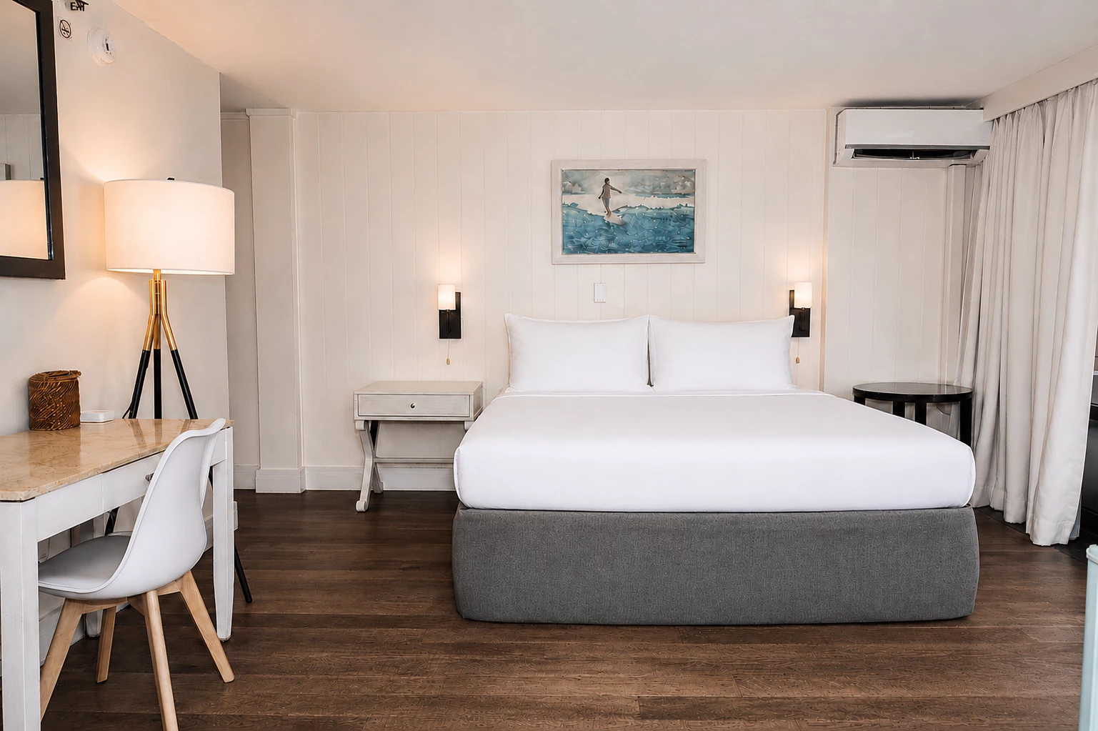 A clean and minimalist hotel room with a large bed, desk, and chair.