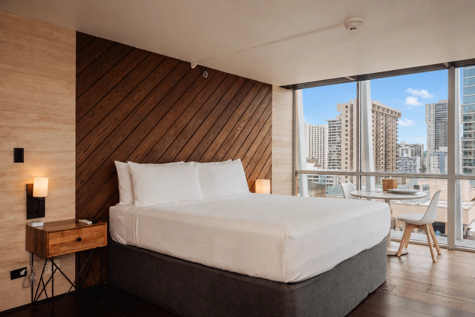 A hotel room with a king-sized bed, a desk, and a city view.