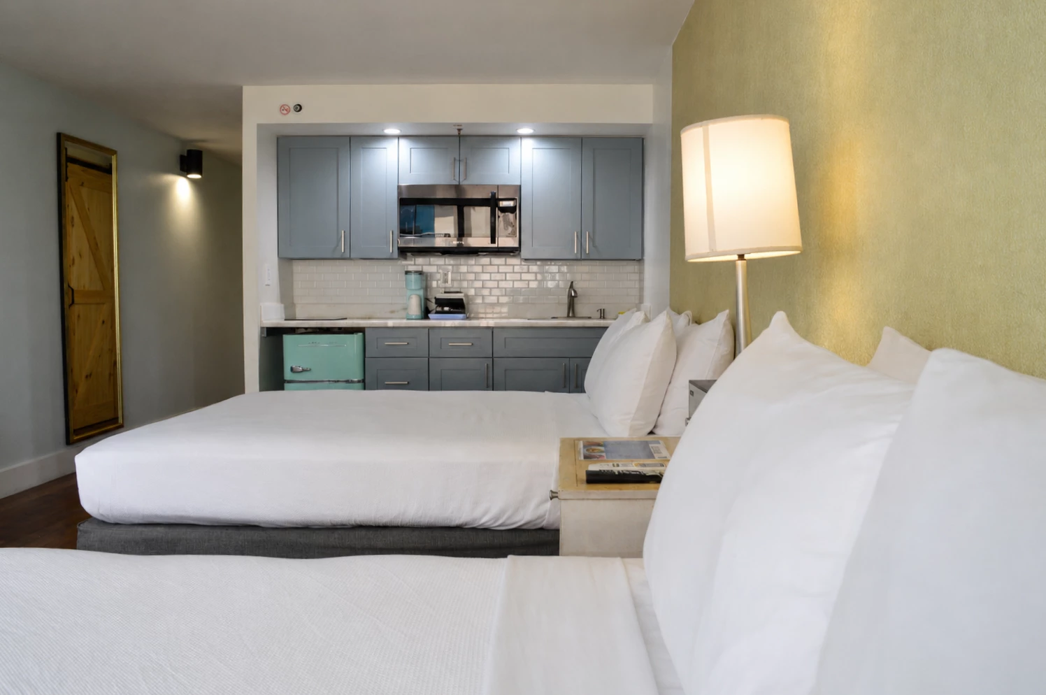 A hotel room with two beds, a kitchenette, and modern appliances.