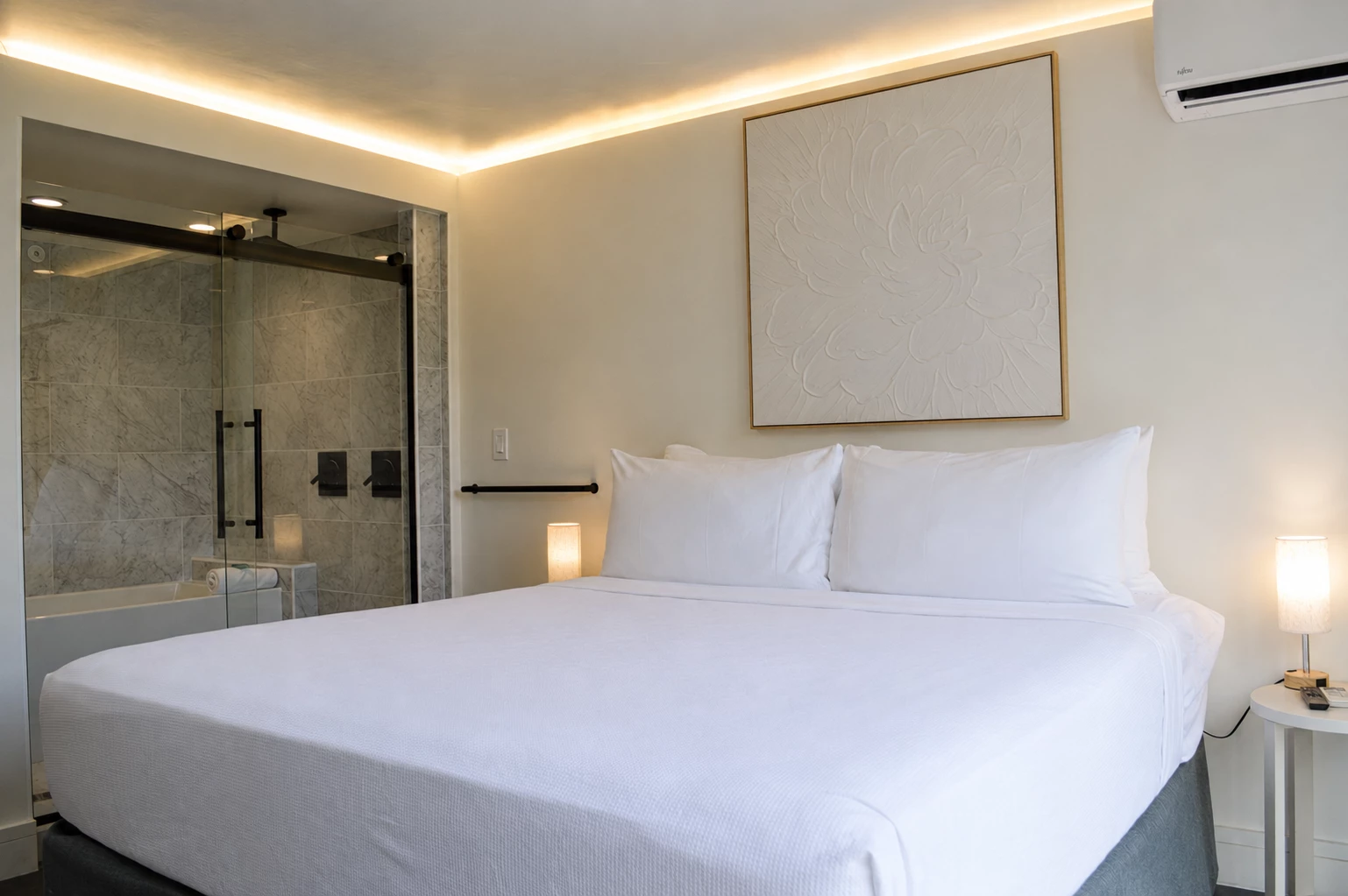 A hotel room with a large bed, a shower and bathtub in an open doorway, and a piece of artwork on the wall.