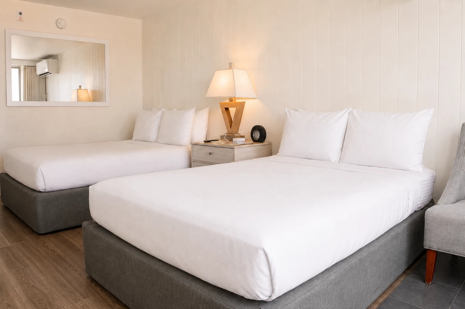 A hotel room with two beds, a mirror, and a lamp.