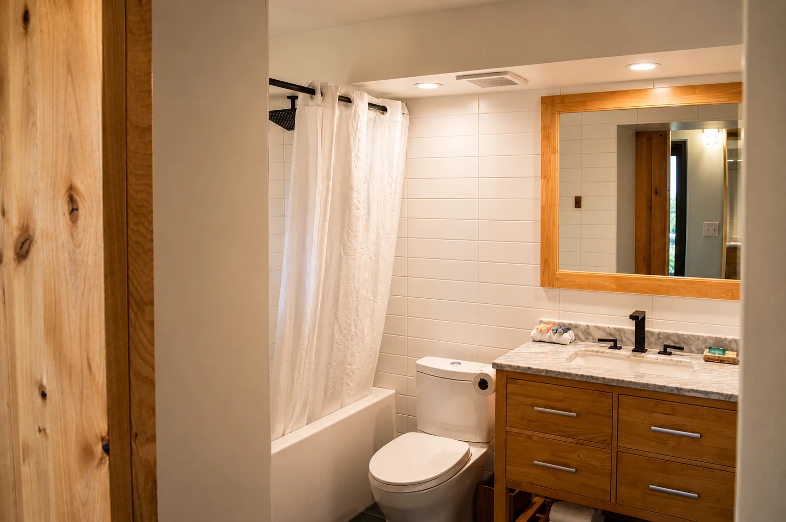A clean bathroom with a wooden vanity, marble countertop, and white tile