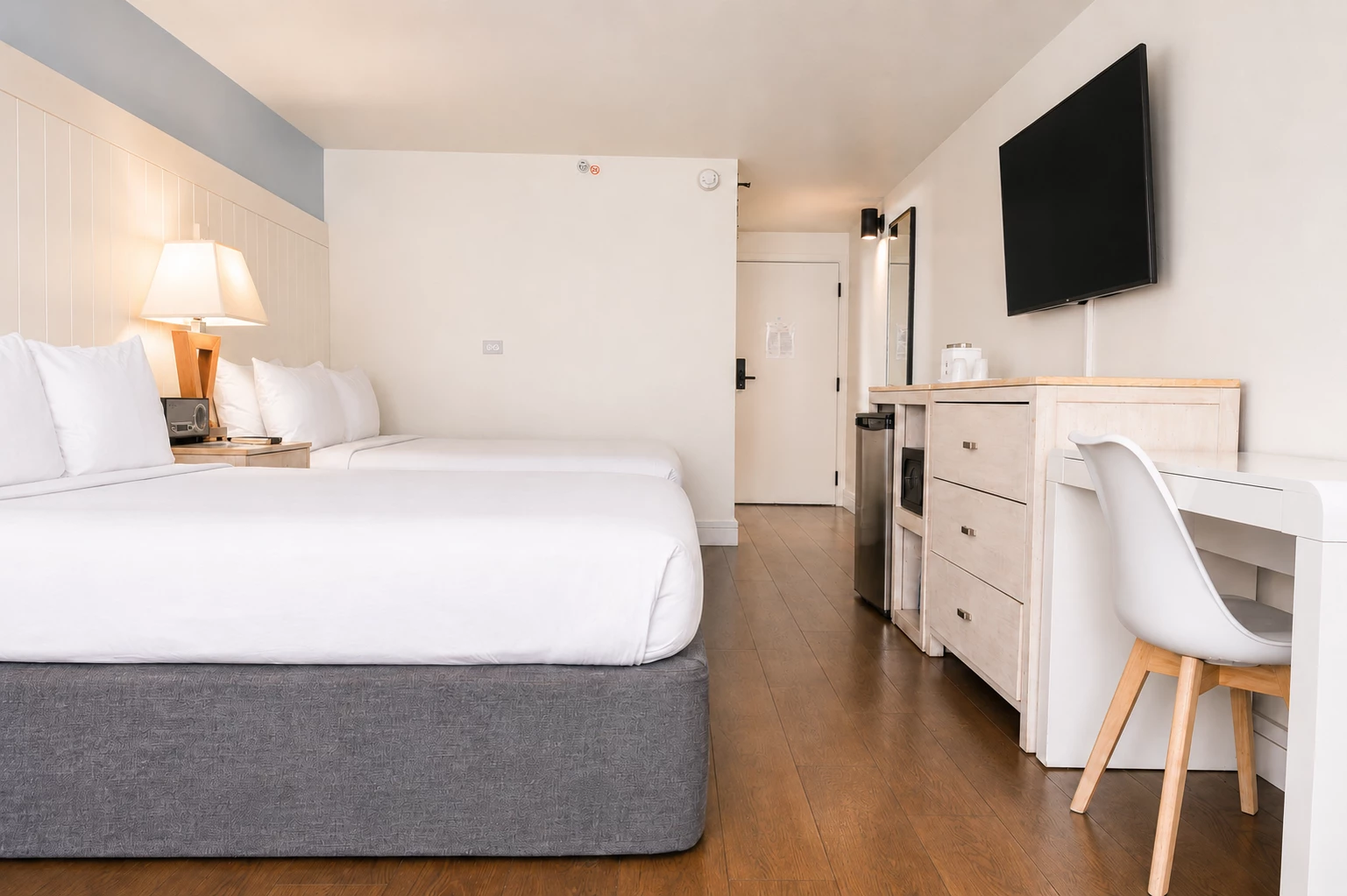A hotel room with two beds, a desk, and a TV.