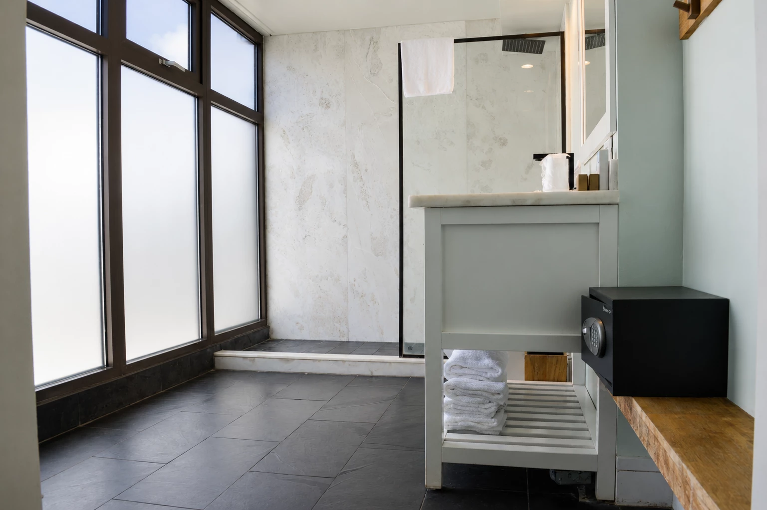 A modern bathroom with a shower, safety box, and towels.