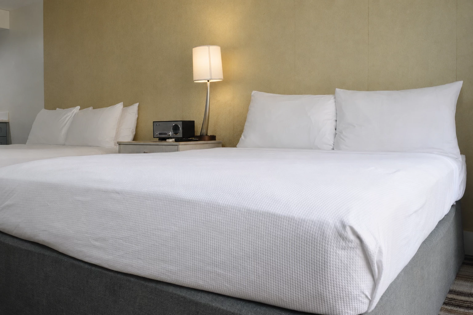 A neatly made bed with white bedding and pillows, a gray bed frame, a lamp, and a radio on a nightstand.