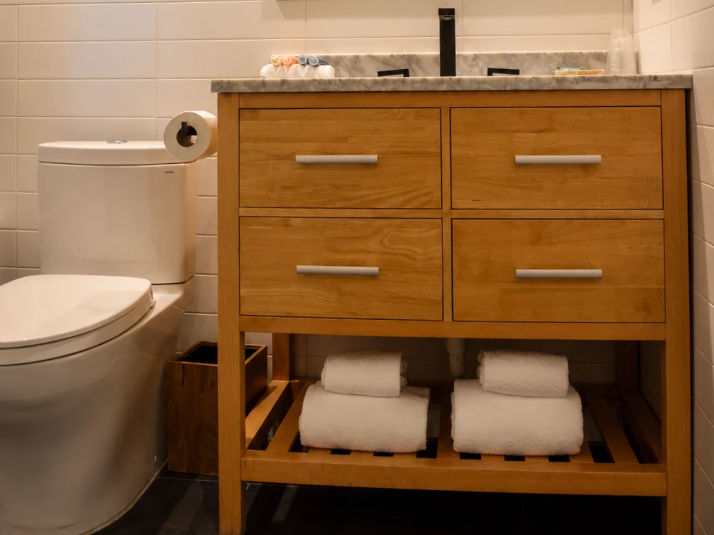 A bathroom vanity with a marble countertop and wooden drawers, next to a toilet.