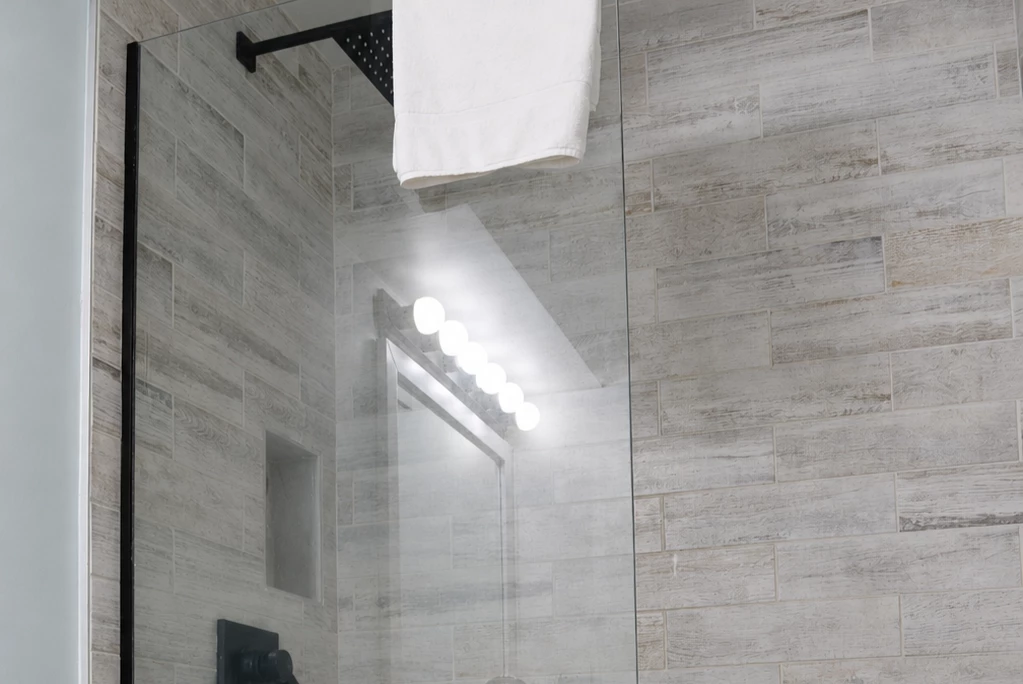 A modern bathroom shower with a glass door, tile walls, and a towel hanging from a rack.