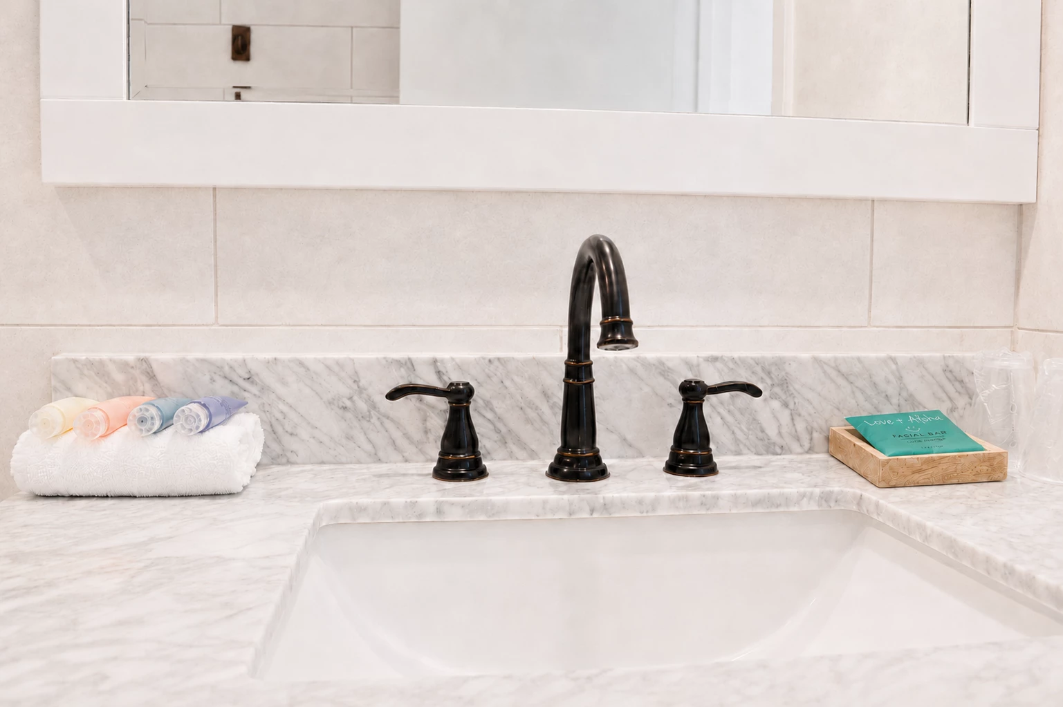 A bathroom sink with a marble countertop, black faucet, and amenities