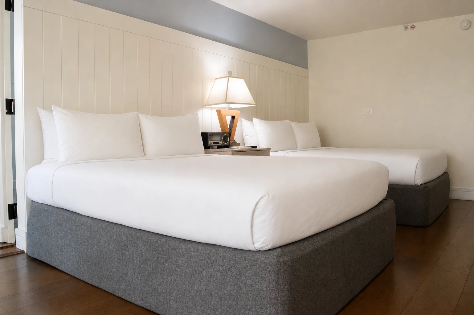 A hotel room with two beds, a nightstand, and a lamp.