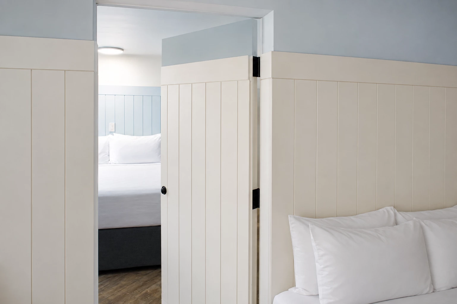 A hotel room with an open door showing a bed with white bedding and a wood floor.
