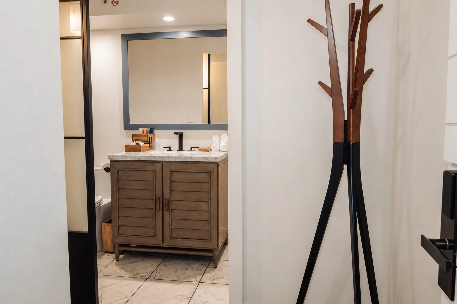 A bathroom with a wooden cabinet, marble countertop, and a coat rack in the corner.