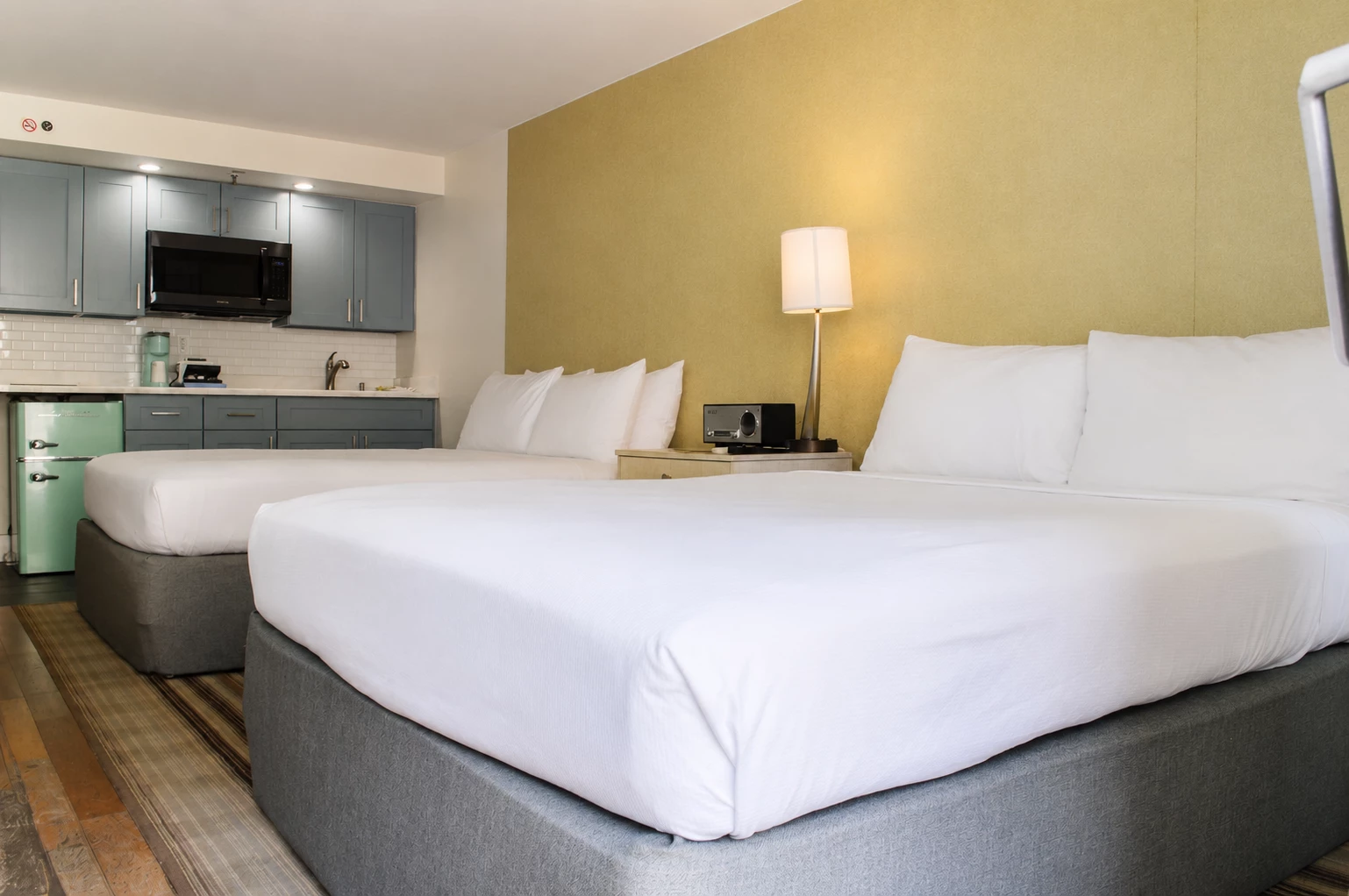 A hotel room with two double beds, a kitchenette, and modern amenities.