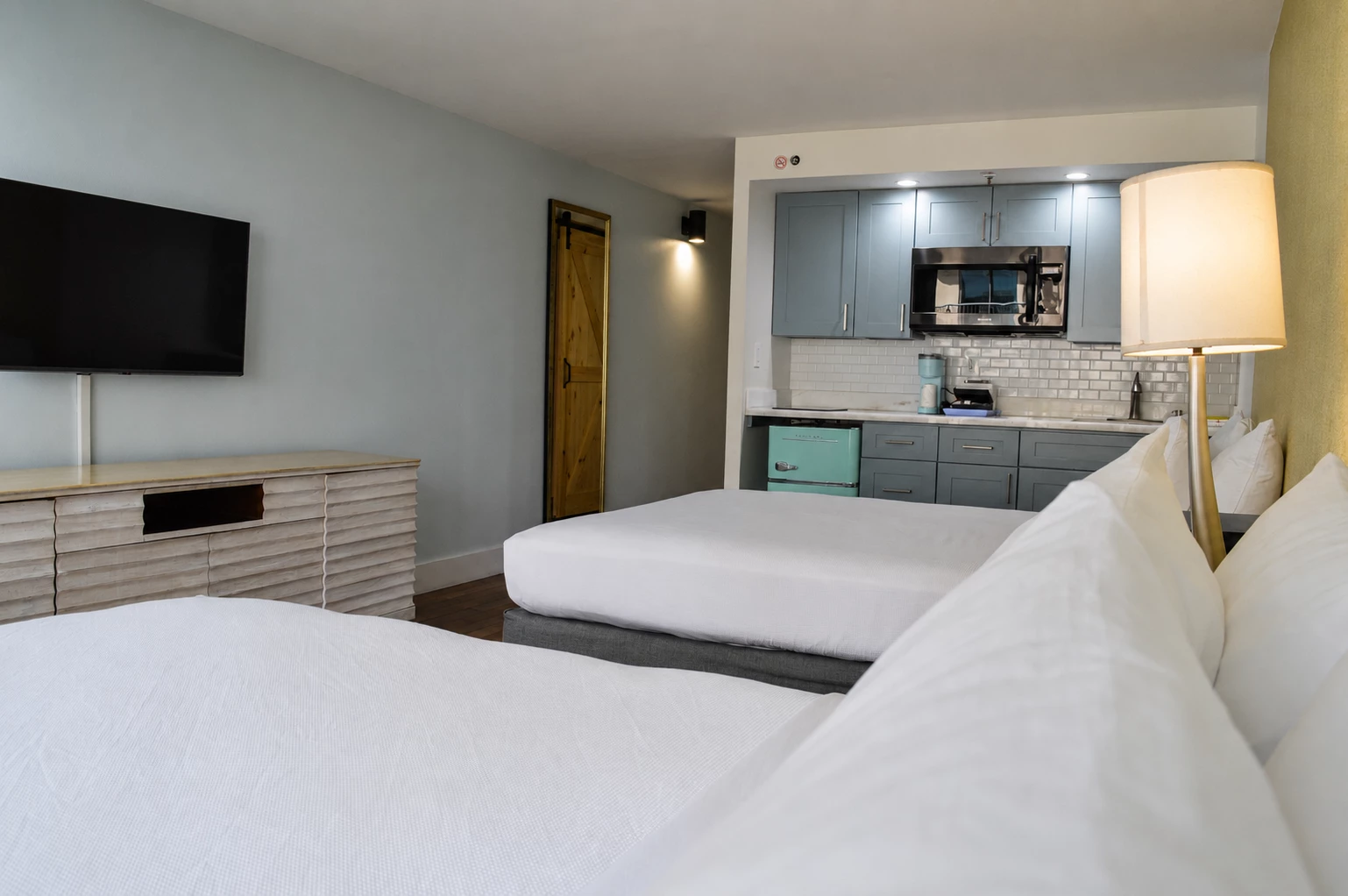 A hotel room with two beds, a kitchenette, and a TV